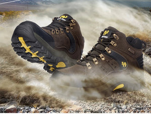 A pair of rugged brown hiking boots with yellow and gold accents, shown kicking up dust on a rocky outdoor trail. The boots feature black and brown panels, gold-tone eyelets, and yellow logo details.