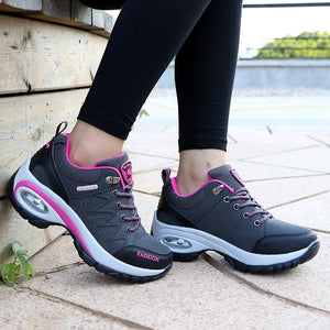 Gray and pink sneakers worn by a person on a wooden floor.