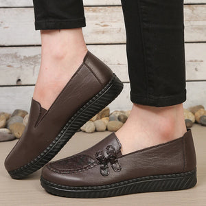 Brown leather shoes worn with black pants on a wooden floor.