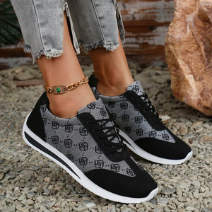 Black and gray patterned sneakers worn with rolled-up jeans on a textured surface.