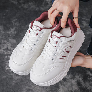 A pair of white platform sneakers with burgundy accents, held by hands against a dark gray textured background.