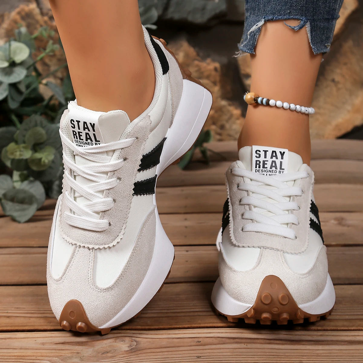 White sneakers with black accents and 'Stay Real' text on a wooden floor.