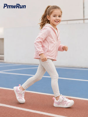 A young girl running on an outdoor track and field wearing a light pink lightweight jacket, light gray leggings, and pink and white sneakers. The PmwRun brand logo is visible in the top left corner.