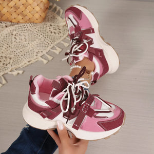 Pink and maroon sneakers with white laces held by a hand on a neutral background