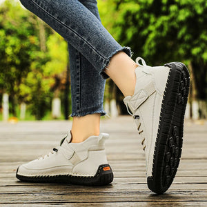 White Slip-On Shoes with black soles worn by a person on a wooden floor with greenery in the background