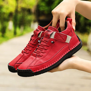 Red sneakers with black soles held by a hand against a blurred green outdoor background