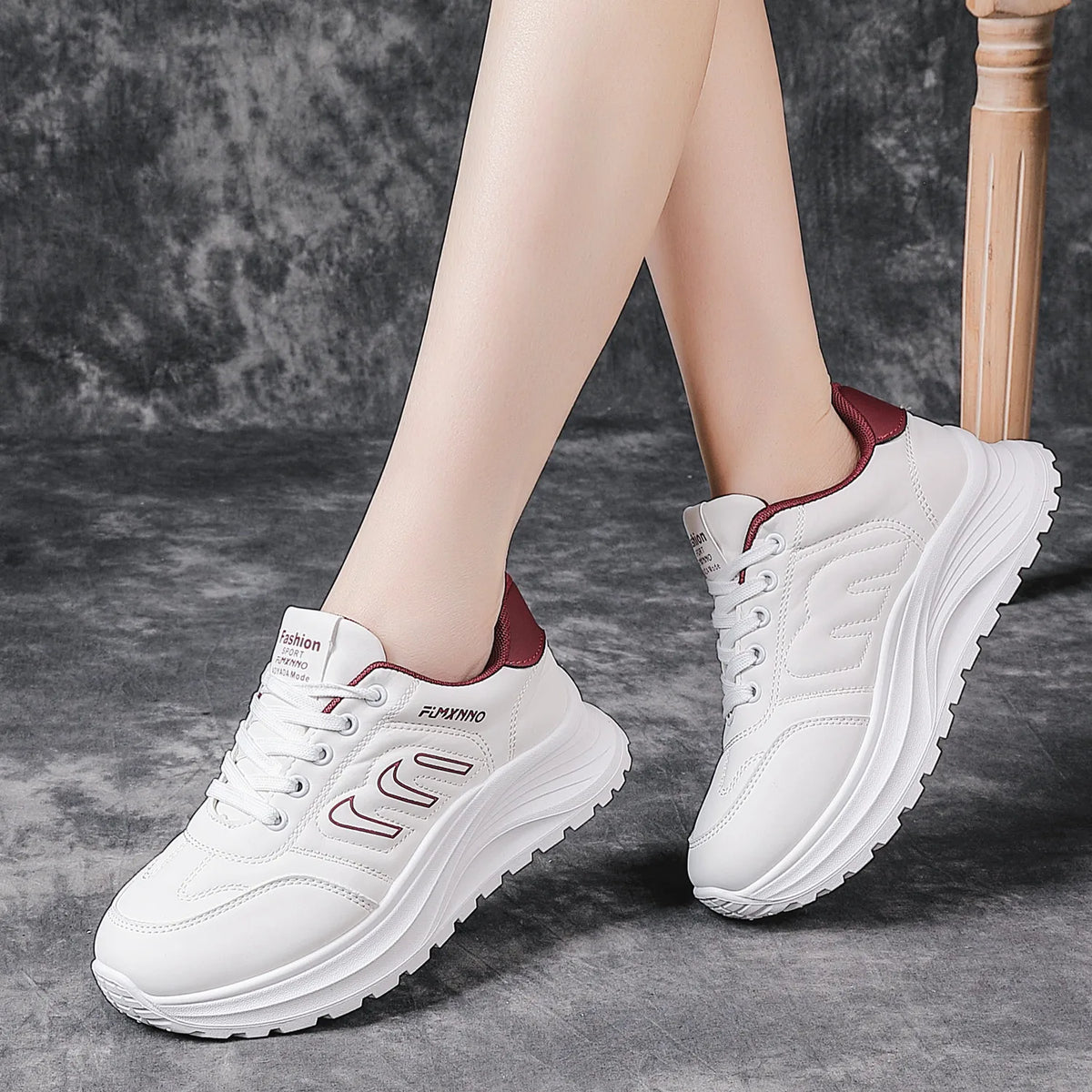 White platform sneakers with burgundy accents, shown on a model's feet against a textured gray background.