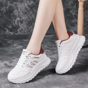 White platform sneakers with burgundy accents, shown on a model's feet against a textured gray background.