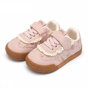 A pair of children's low-top sneakers in light pink suede and faux leather, featuring cream lace trim, hook-and-loop straps, and brown rubber soles.