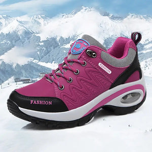 A pink and black winter hiking shoe with a white midsole, shown in a snowy mountain landscape. The shoe features pink laces, a pink and black toe cap, and the word 'FASHION' printed on the side and tongue.
