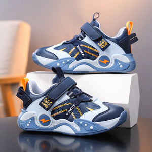 A pair of children's athletic sneakers in navy blue, light blue, and white, with yellow and orange accents. One shoe is placed in front of the other on a white box, set against a softly blurred indoor background.