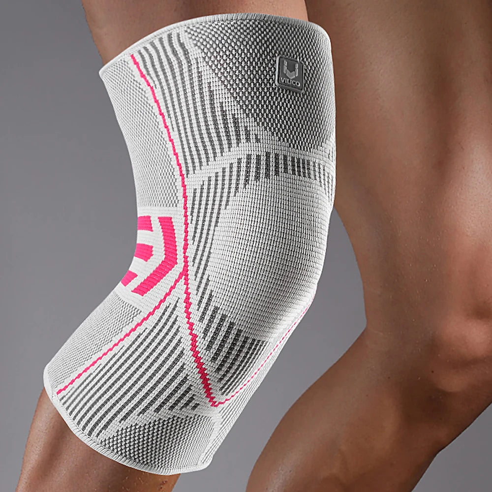White knee brace with pink accents on a person's knee against a gray background
