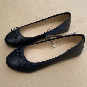 Pair of black ballet flats with bow details on a beige surface