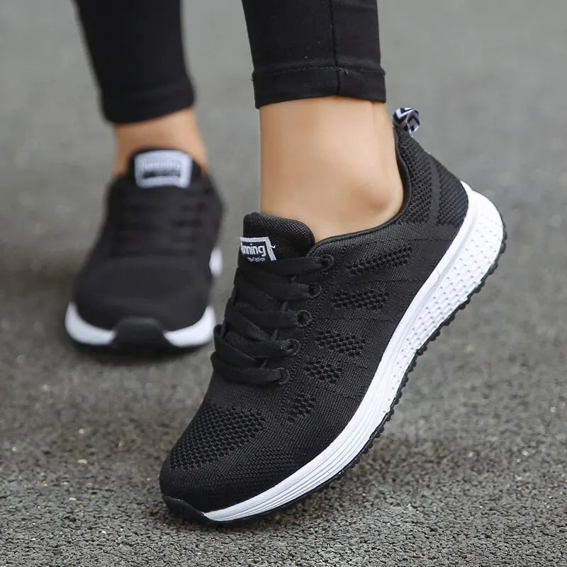 Black running shoes with white soles worn by a person on a gray surface