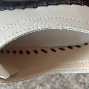 Close-up of a white leather shoe with black stitching on a textured surface.