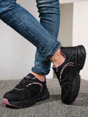 Black chunky platform sneakers with pink accents, shown on a model wearing blue jeans.