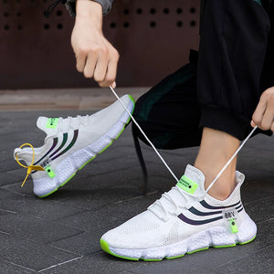 Person tying white sneakers with green accents on a dark floor.