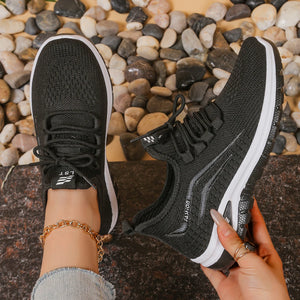Black running shoes with white soles held by a person on a pebble surface