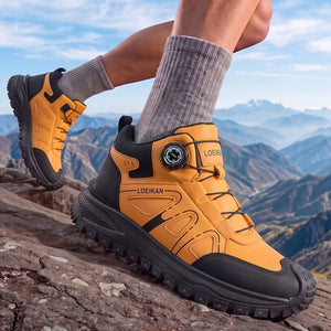 A person wearing a pair of LoEikan hiking shoes with a dial closure, standing on a rocky mountain peak with a scenic mountain range and blue sky in the background.