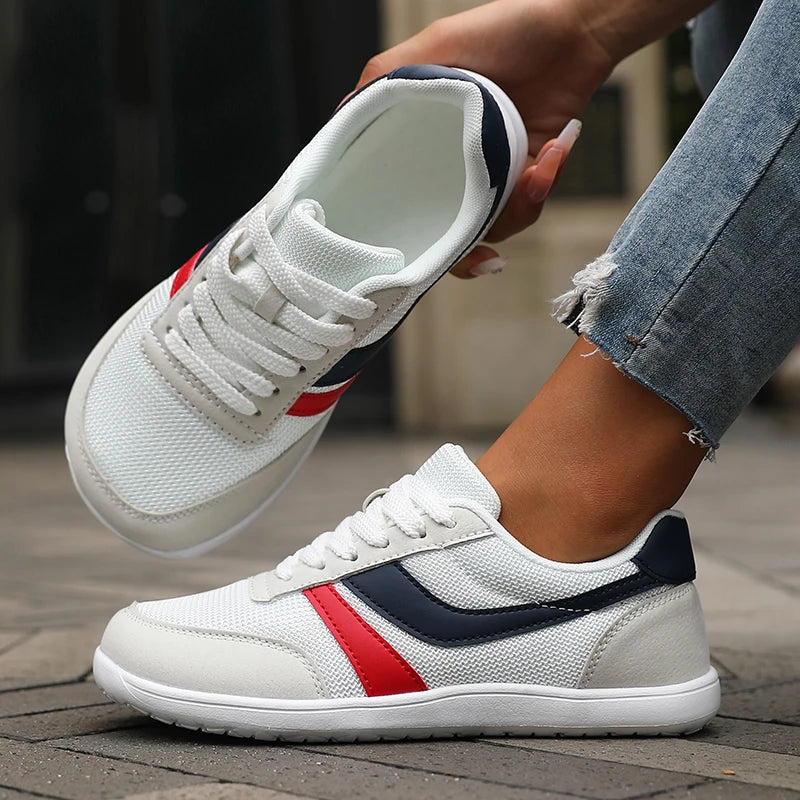White sneakers with red and blue stripes worn by a person on a wooden floor.