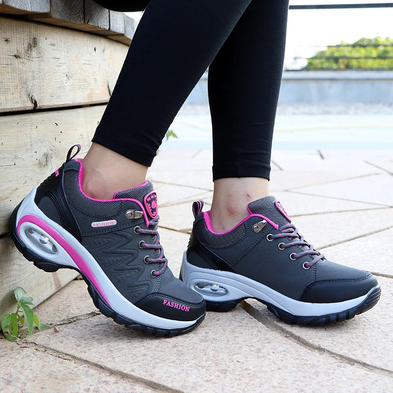 Gray and pink sneakers worn by a person on a wooden floor.