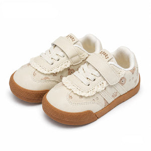 A pair of toddler sneakers in cream canvas with lace trim, hook-and-loop straps, and brown rubber soles, shown on a white background.