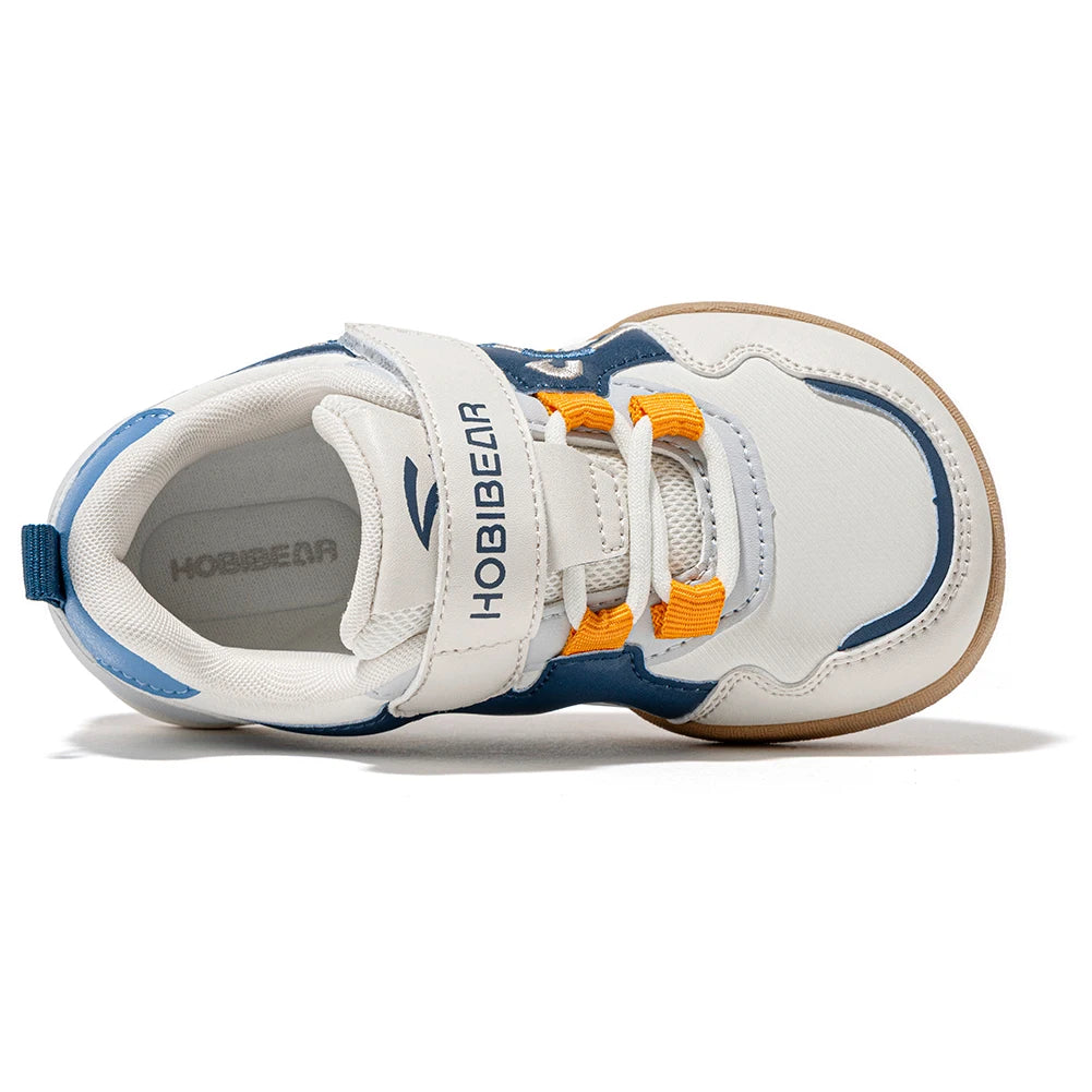 A children's white sneaker with navy blue panels, orange laces, and a tan outsole, shown from a side profile on a white background. The brand name HOBIBEAR is visible on the strap and the inner sole.