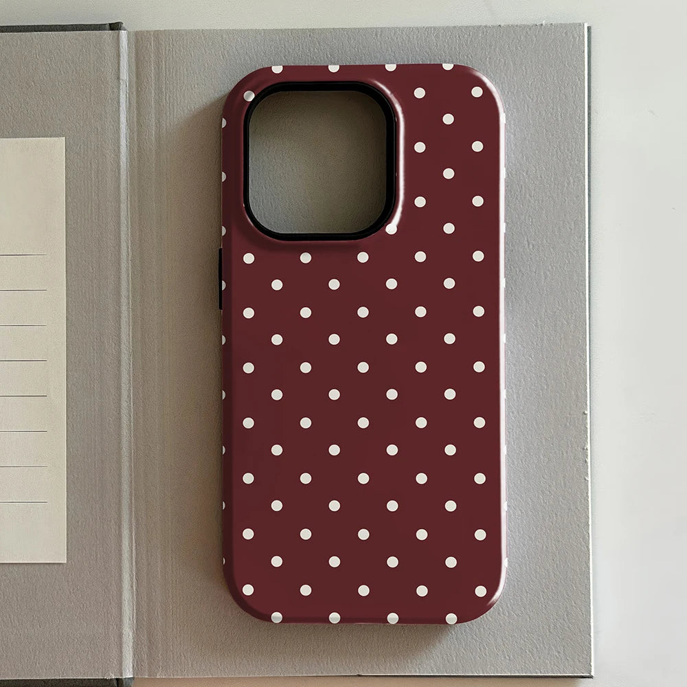 iPhone case with white polka dots on a red background, placed on an open book.