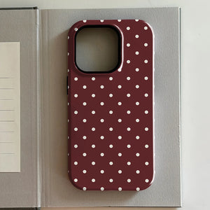 iPhone case with white polka dots on a red background, placed on an open book.