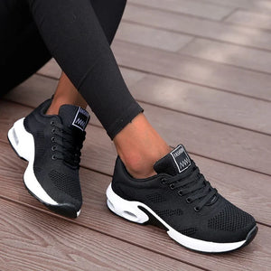 A woman modeling a black long-sleeve athletic top and matching black leggings with black sneakers, photographed against a clean white studio background.