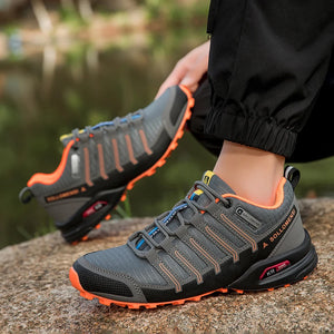 Gray and orange hiking shoes worn by a person sitting on a rock with a blurred natural background