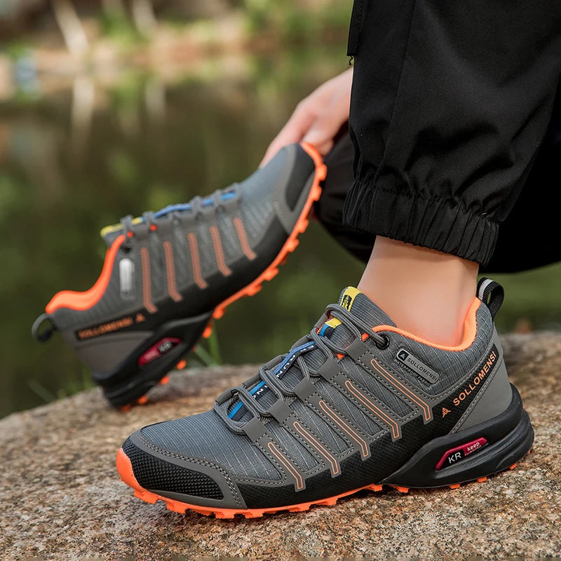 Gray and orange hiking shoes worn by a person sitting on a rock with a blurred natural background