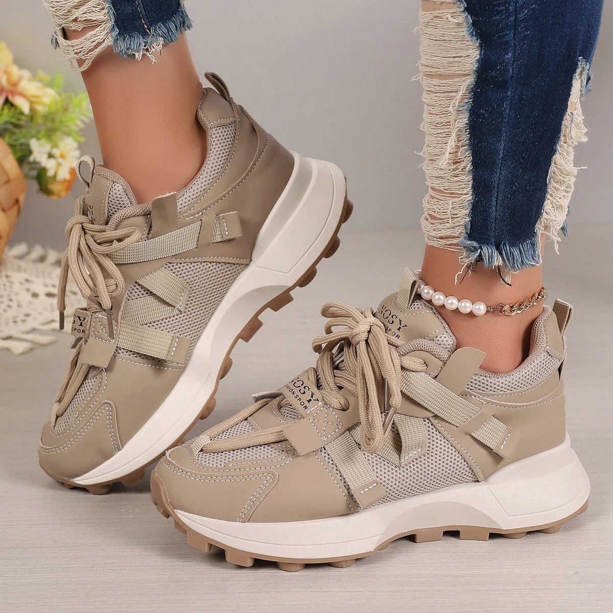 Beige sneakers worn with ripped jeans on a neutral background