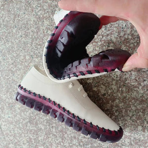 White boot with maroon soles held by a hand on a textured surface