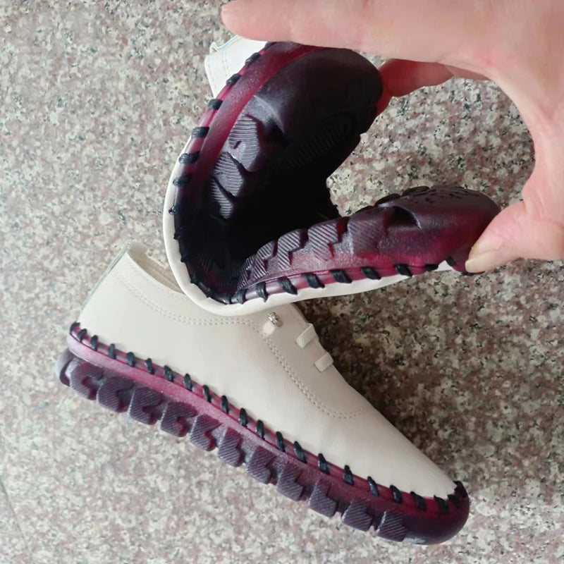 White boot with maroon soles held by a hand on a textured surface