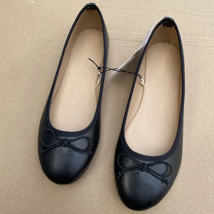 Pair of black flat shoes with a bow on a beige background