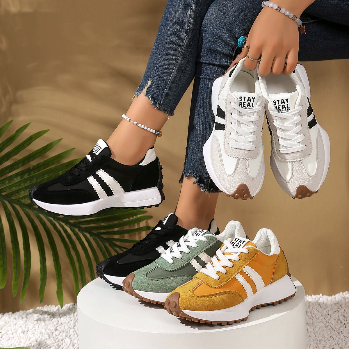 Four pairs of sneakers in black, white, green, and brown on a white platform with a blurred background.