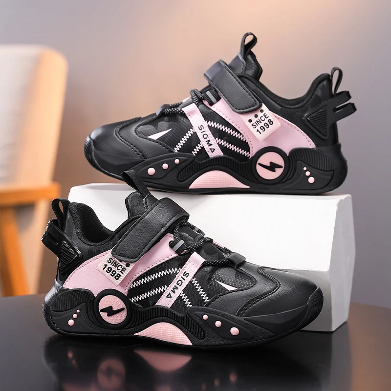 A pair of black and pink children's sneakers displayed on a white box against a softly blurred indoor background. The shoes feature hook-and-loop straps, textured synthetic panels, and decorative text accents including 'SINCE 1986' and 'SIGMA'.