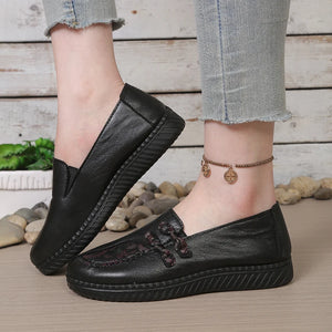 Black loafers worn with light blue jeans on a wooden floor.