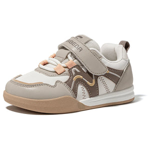 A children's low-top sneaker by BCBear in a neutral color palette. The shoe features light gray and white panels, taupe brown overlays, peach-colored elastic laces, and a tan outsole, shown from a three-quarters angle on a white background.