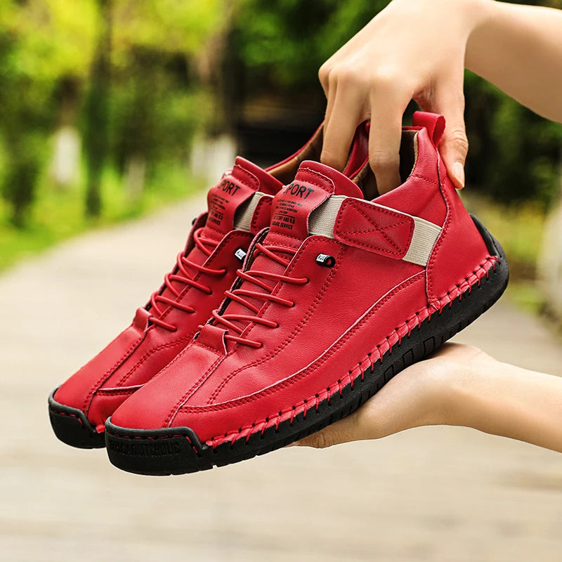 Red sneakers with black soles held by a hand against a blurred green outdoor background