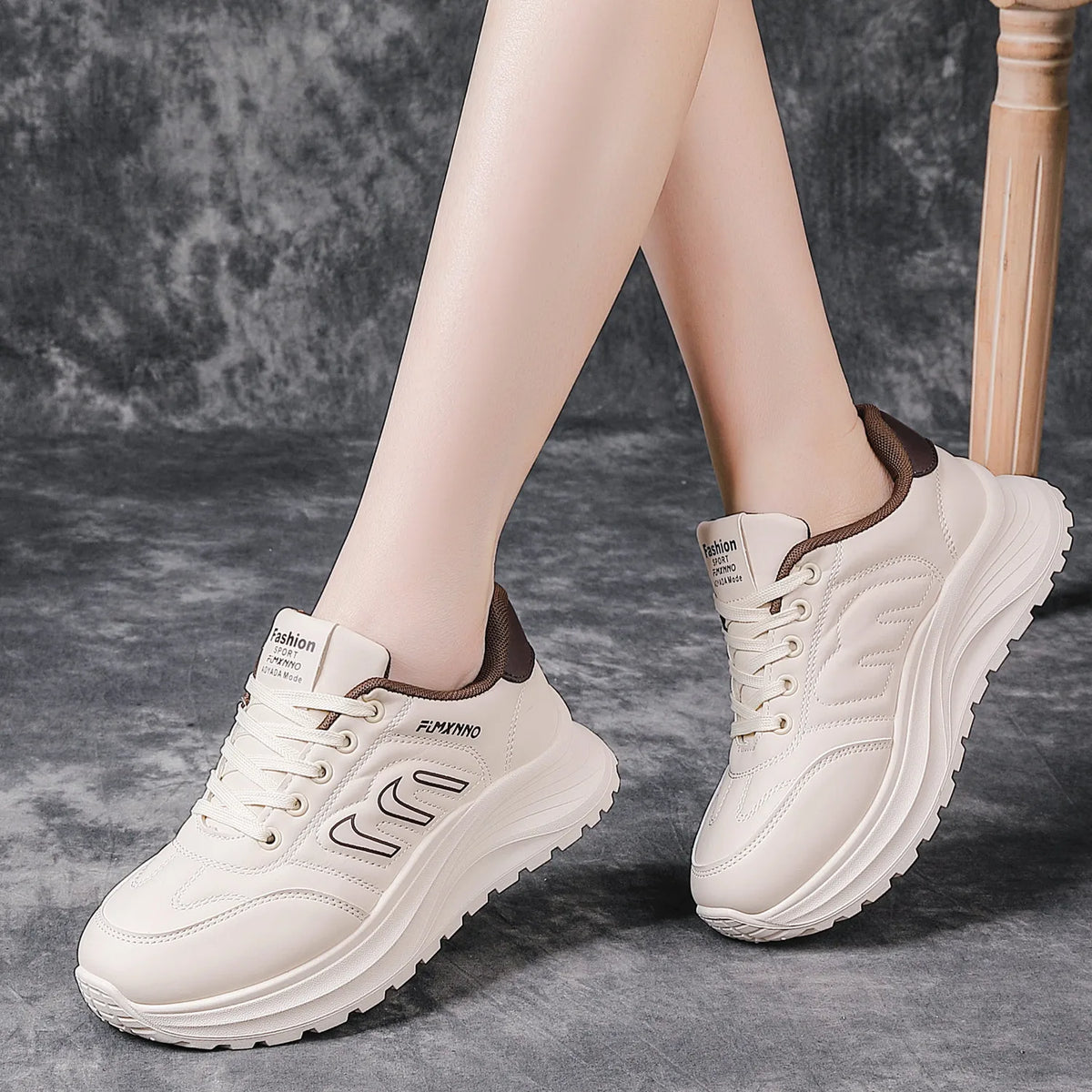 A pair of chunky platform sneakers in off-white with brown accents, shown on a model's feet against a textured gray background.