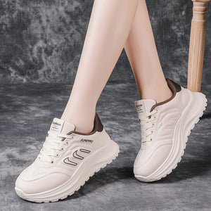 A pair of chunky platform sneakers in off-white with brown accents, shown on a model's feet against a textured gray background.