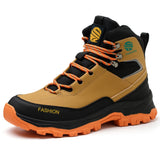 A mid-cut safety boot with a tan and black upper, orange laces and outsole, and silver metal eyelets, shown on a white background.