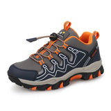 A gray and navy outdoor hiking shoe with bright orange accents, featuring a lace-up design, white wave-like stitching details, and a rugged sole.