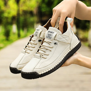 White sneakers with black soles held by a hand against a blurred green outdoor background