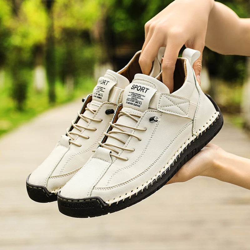 White sneakers with black soles held by a hand against a blurred green outdoor background