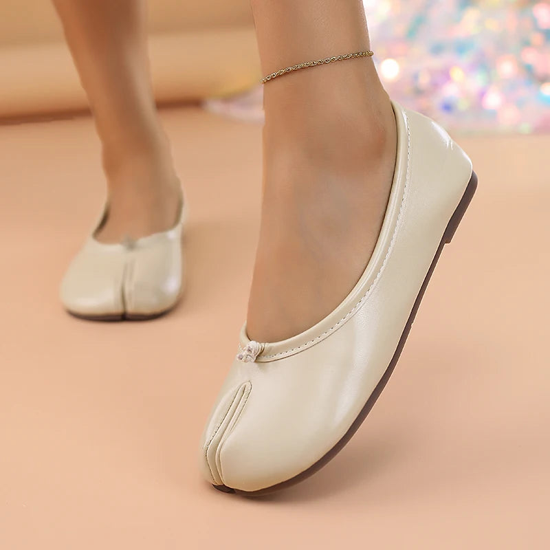 White flat shoes worn on a beige surface with a blurred colorful background