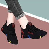 Black slip-on shoes with colorful accents worn by a person on a multicolored background