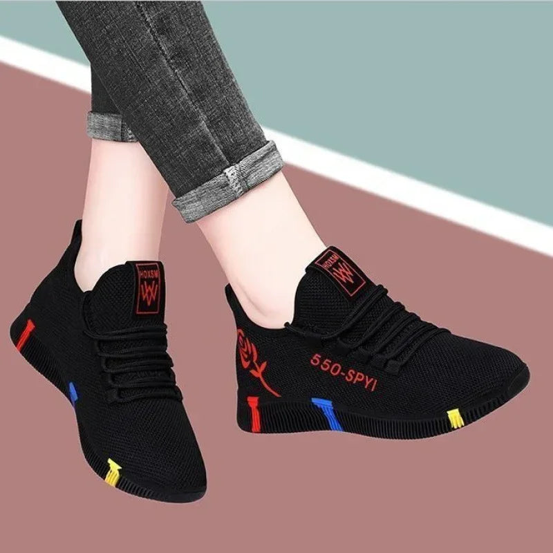 Black slip-on shoes with colorful accents worn by a person on a multicolored background